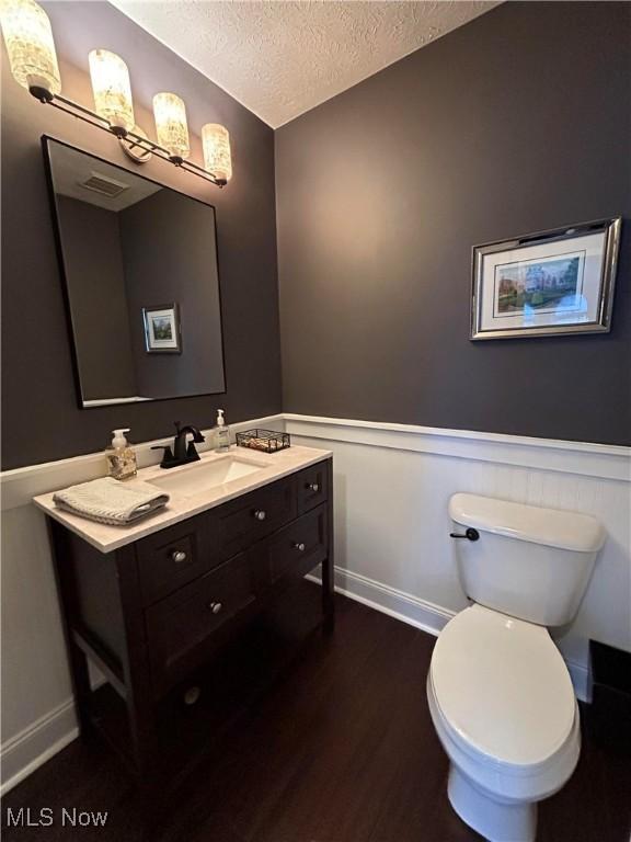 bathroom featuring a textured ceiling, toilet, wood finished floors, vanity, and wainscoting