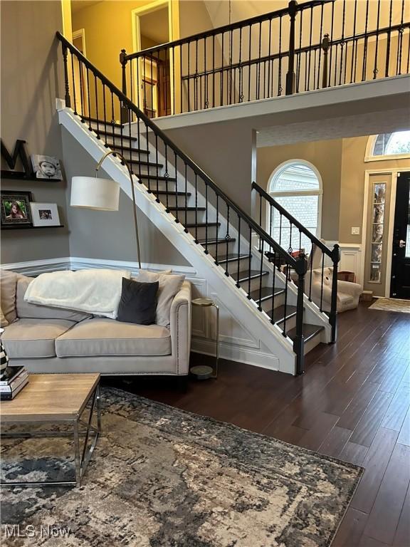 living area with stairs, a high ceiling, wainscoting, and wood finished floors