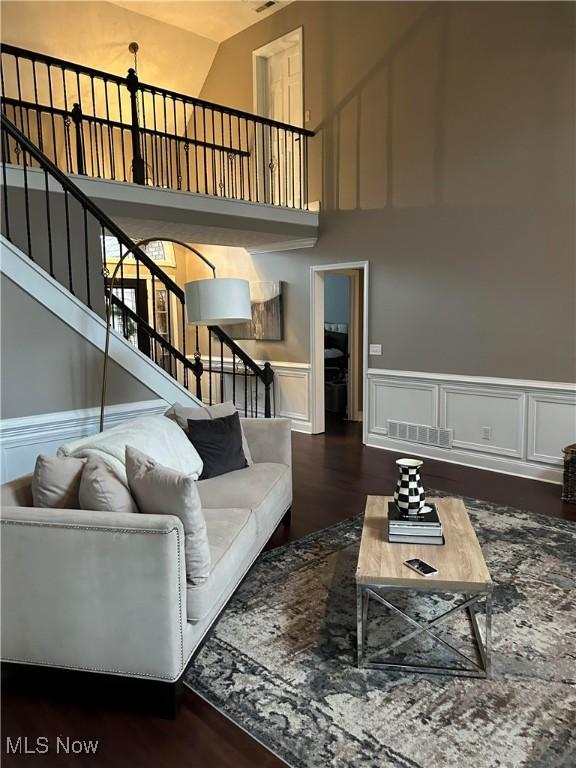 living room featuring visible vents, a decorative wall, wainscoting, wood finished floors, and stairs