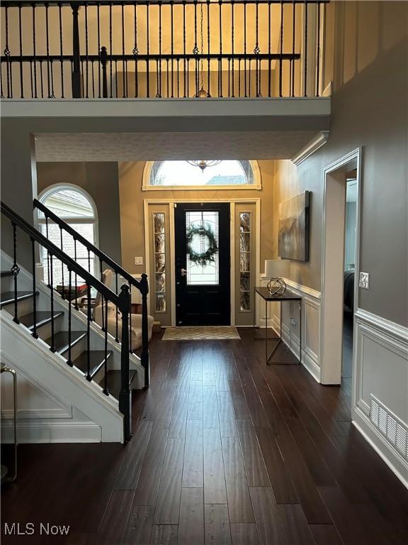 entrance foyer featuring a decorative wall, a wainscoted wall, dark wood-style flooring, a towering ceiling, and stairs