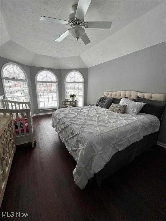 bedroom featuring baseboards, a textured ceiling, a tray ceiling, and dark wood-style flooring