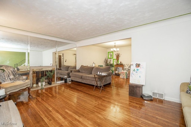 living area featuring visible vents, a notable chandelier, a textured ceiling, and wood finished floors