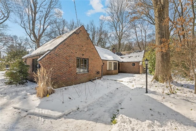 snow covered property featuring brick siding and a chimney