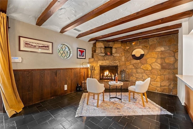 sitting room with a wainscoted wall, wood walls, a fireplace, beam ceiling, and stone finish floor