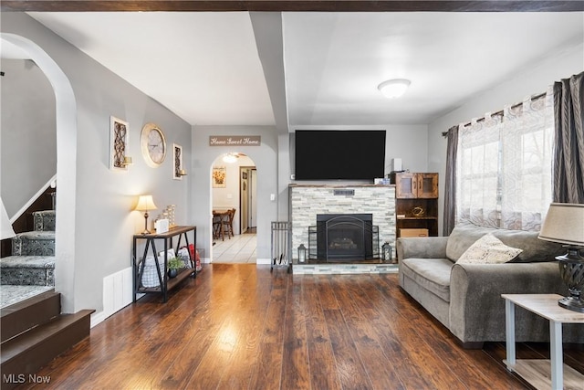 living room featuring arched walkways, visible vents, stairway, a stone fireplace, and hardwood / wood-style flooring