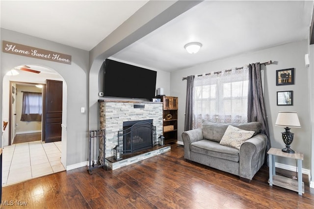 living area with baseboards, arched walkways, wood finished floors, and a stone fireplace