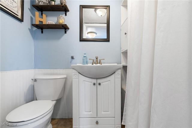 bathroom with a wainscoted wall, vanity, and toilet