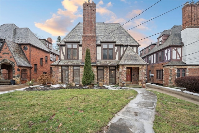 tudor-style house with a yard, a chimney, and stucco siding