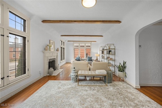 living room with arched walkways, beamed ceiling, wood finished floors, a textured ceiling, and a wealth of natural light