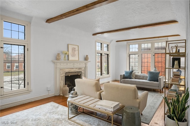 living area featuring beam ceiling, a premium fireplace, a textured ceiling, wood finished floors, and plenty of natural light