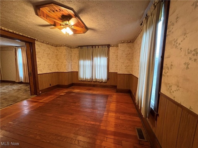 unfurnished room with a textured ceiling, hardwood / wood-style floors, wainscoting, and wallpapered walls