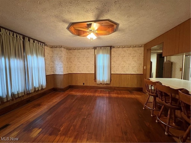 empty room with dark wood-type flooring, wainscoting, ceiling fan, and a textured ceiling