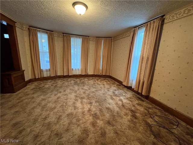 carpeted empty room with a textured ceiling, baseboards, and wallpapered walls