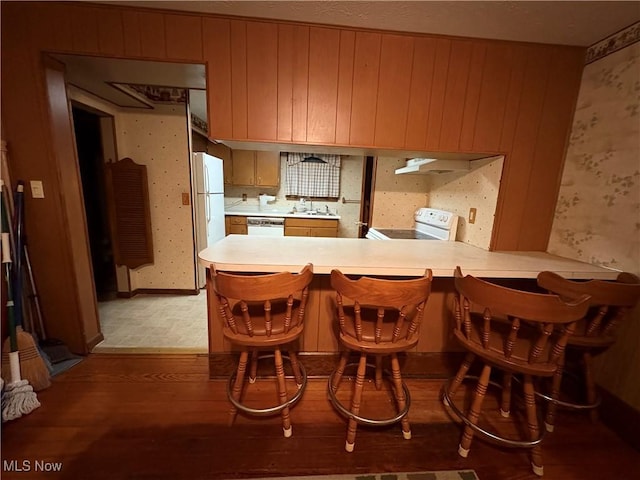 kitchen with a peninsula, white appliances, a sink, light countertops, and wallpapered walls