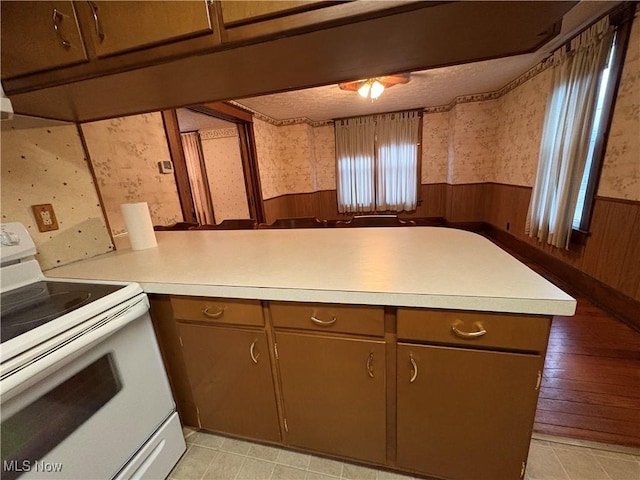 kitchen with electric stove, wainscoting, a peninsula, and wallpapered walls