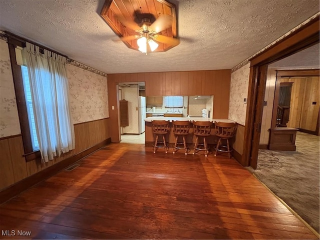 unfurnished dining area featuring a wainscoted wall, visible vents, a textured ceiling, and hardwood / wood-style flooring