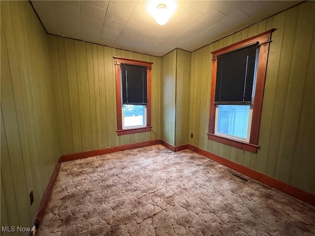 unfurnished room with carpet floors, wooden walls, visible vents, and baseboards