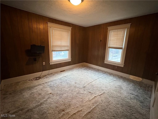 spare room featuring carpet flooring, wood walls, a textured ceiling, and baseboards