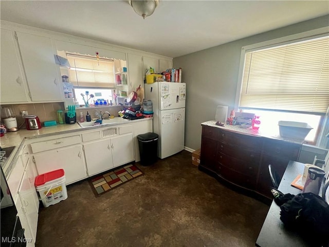 kitchen with light countertops, freestanding refrigerator, white cabinets, a sink, and concrete flooring