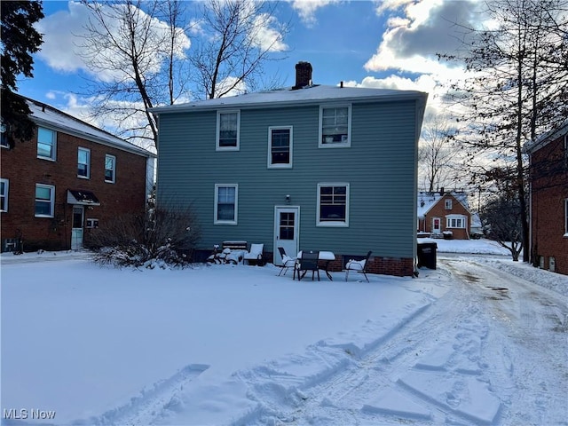 snow covered rear of property with a chimney