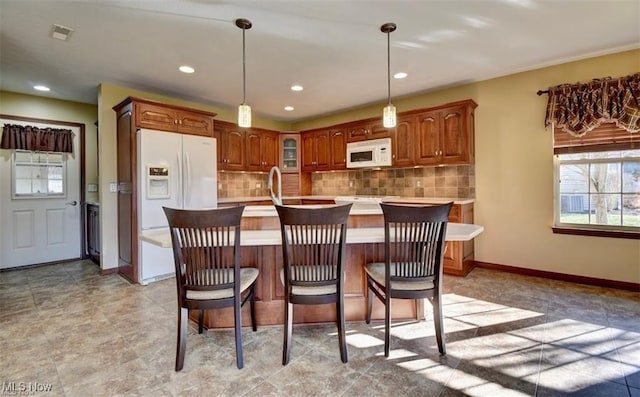 kitchen with light countertops, backsplash, a kitchen island with sink, white appliances, and baseboards