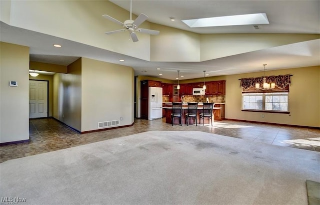 unfurnished living room with high vaulted ceiling, carpet, a skylight, and visible vents