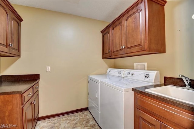 washroom with a sink, washing machine and dryer, cabinet space, and baseboards