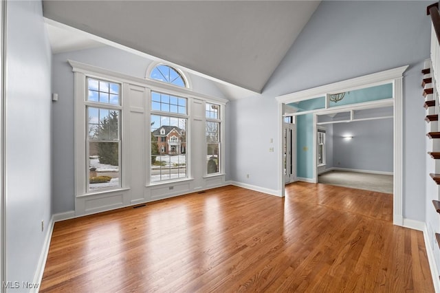 unfurnished room with high vaulted ceiling, plenty of natural light, and wood finished floors