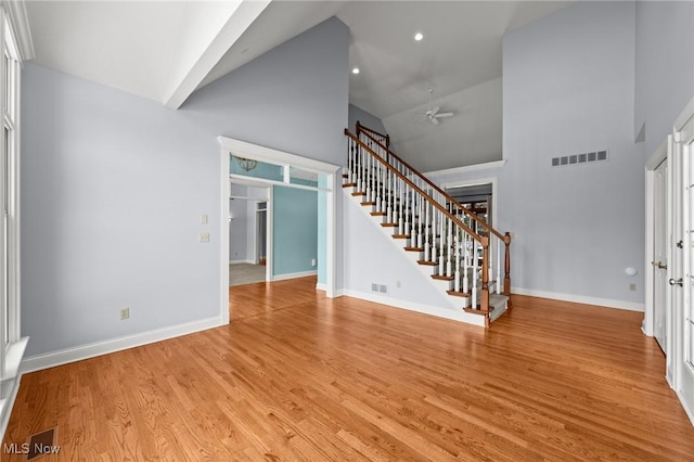 interior space featuring light wood finished floors, stairs, visible vents, and high vaulted ceiling