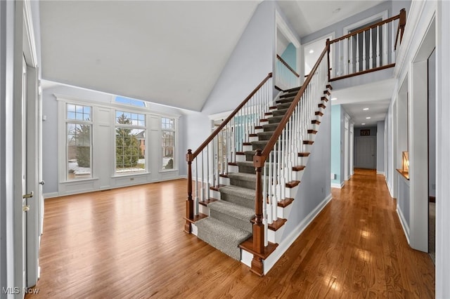 foyer with stairway, wood finished floors, a towering ceiling, and baseboards