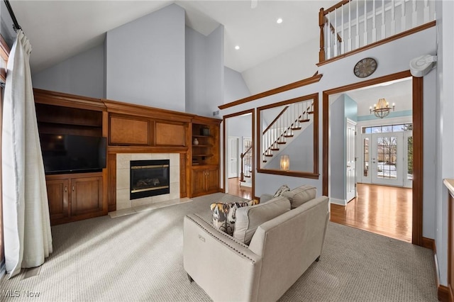 living area featuring a chandelier, high vaulted ceiling, carpet, stairway, and a tiled fireplace