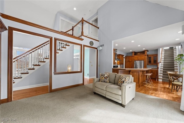 living area featuring recessed lighting, a high ceiling, baseboards, stairs, and light wood finished floors