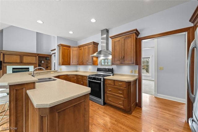 kitchen with light countertops, wall chimney range hood, gas stove, and a sink