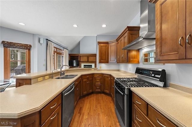 kitchen featuring stainless steel appliances, light countertops, a sink, wall chimney range hood, and a peninsula