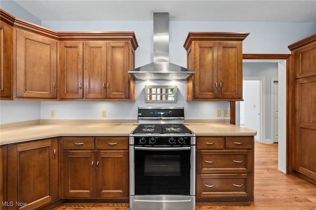 kitchen featuring wall chimney exhaust hood, wood finished floors, light countertops, and range with gas stovetop