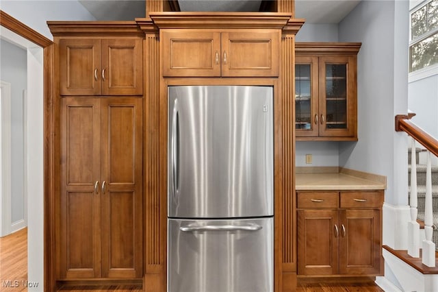 kitchen featuring glass insert cabinets, brown cabinets, light countertops, and freestanding refrigerator