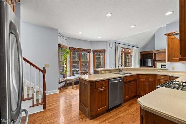 kitchen with a peninsula, a sink, light wood-style floors, appliances with stainless steel finishes, and brown cabinetry