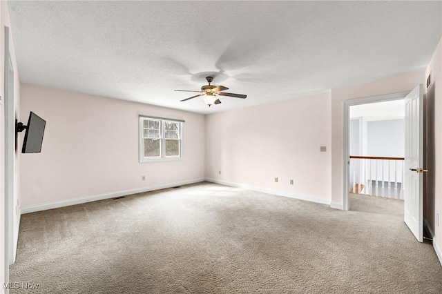 spare room with a ceiling fan, carpet, baseboards, and a textured ceiling