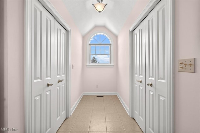 hallway featuring vaulted ceiling, baseboards, and light tile patterned floors