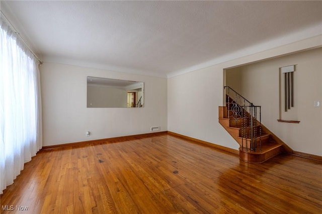 spare room with baseboards, hardwood / wood-style floors, and stairs