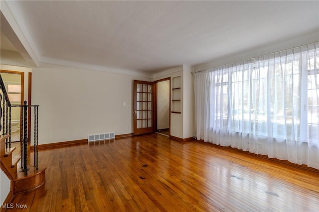 unfurnished room featuring visible vents, stairway, baseboards, and wood finished floors