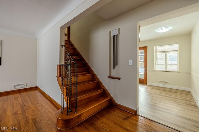 stairway featuring wood finished floors, visible vents, and baseboards