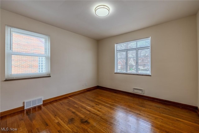 unfurnished room with baseboards, visible vents, and hardwood / wood-style floors