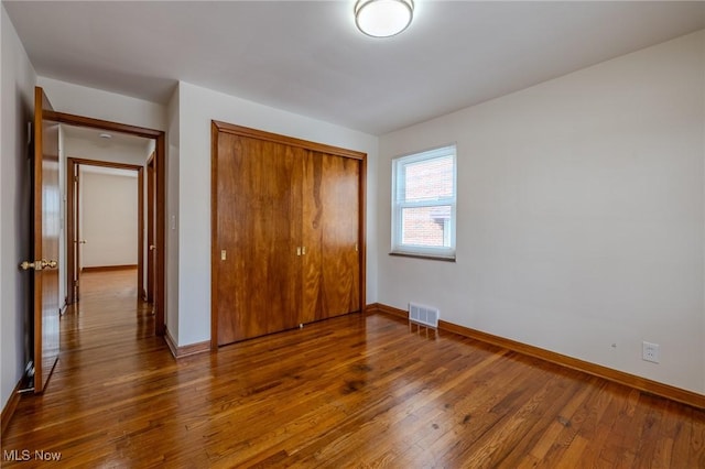 unfurnished bedroom featuring baseboards, wood-type flooring, visible vents, and a closet