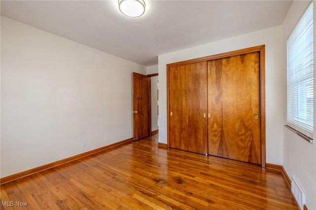 unfurnished bedroom featuring a closet, visible vents, baseboards, and wood finished floors