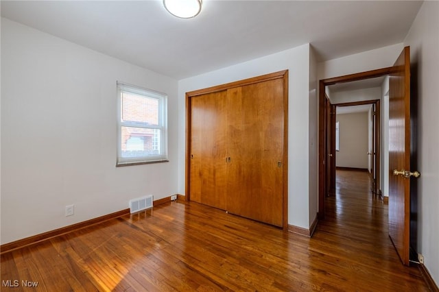 unfurnished bedroom featuring a closet, wood-type flooring, visible vents, and baseboards