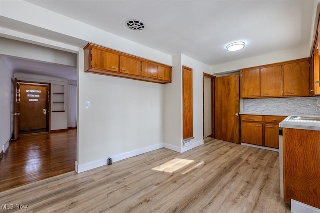 kitchen with brown cabinetry, light countertops, decorative backsplash, and light wood finished floors