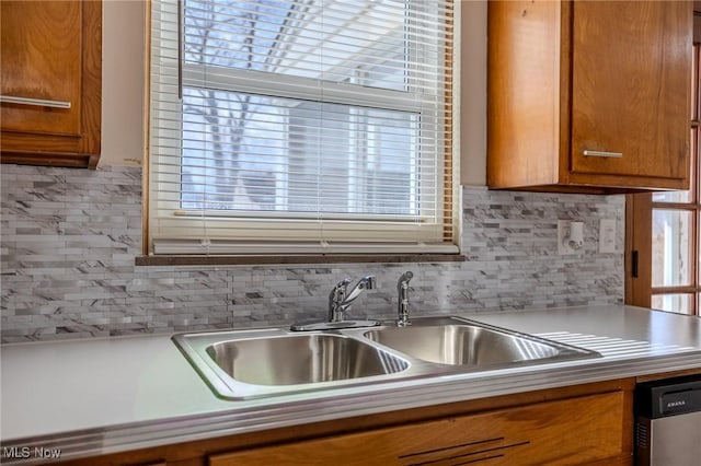 kitchen with a sink, light countertops, stainless steel dishwasher, tasteful backsplash, and brown cabinetry