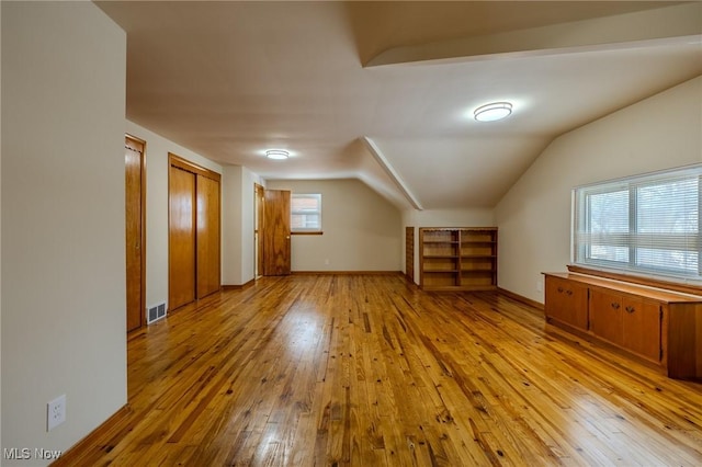 additional living space featuring vaulted ceiling, hardwood / wood-style floors, visible vents, and baseboards