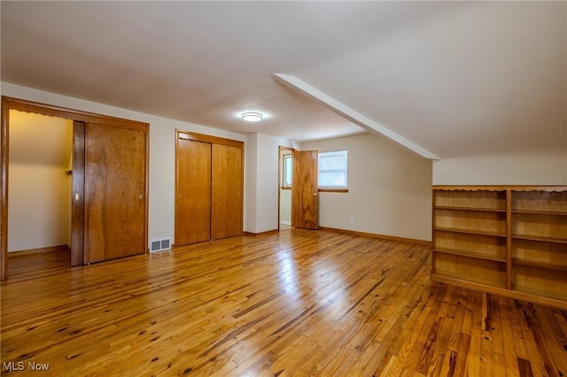 unfurnished bedroom with baseboards, wood-type flooring, visible vents, and multiple closets